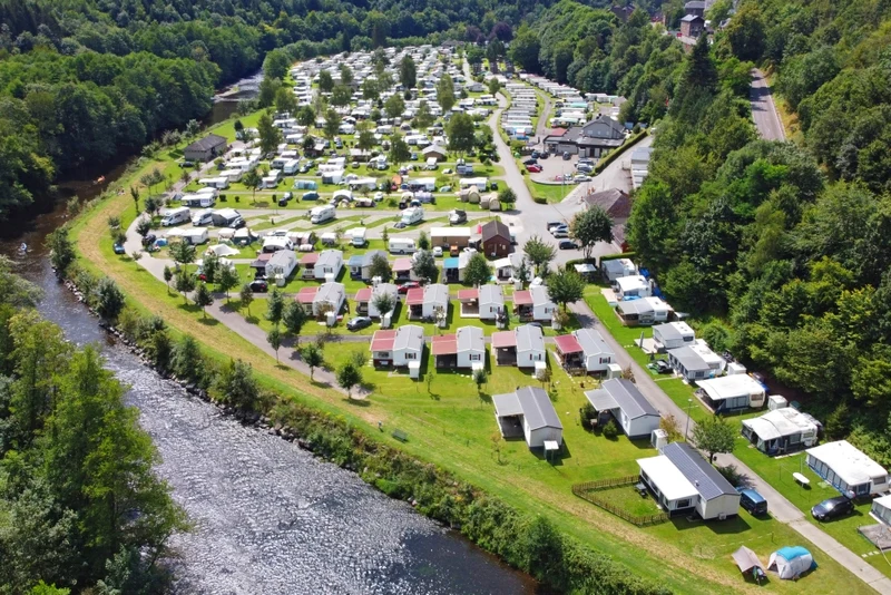 Riverside campsite with caravans and mobile homes nestled among lush green trees, creating a picturesque retreat at Floreal la Roche