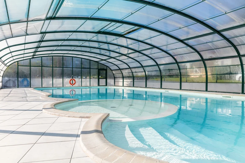 An indoor swimming pool, covered by a glass arch structure, surrounded by tiled flooring at Marvilla Parks La Vallée
