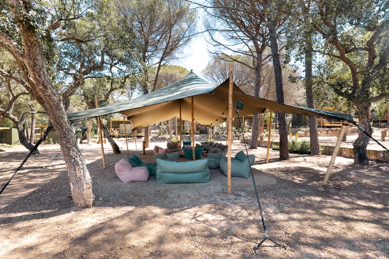 Large outdoor canopy covering colorful lounge chairs, placed among tall trees at Wecamp Santa Cristina