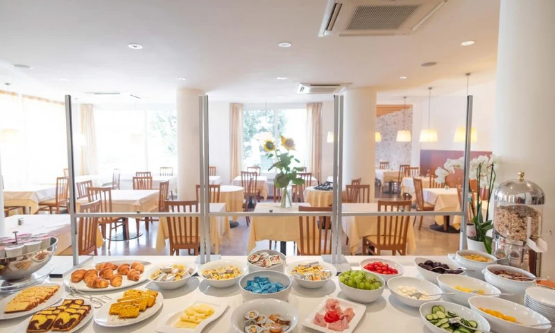 Buffet table with various breakfast foods, set in a bright dining area, featuring tables, chairs, and sunflowers at Hotel Romeo