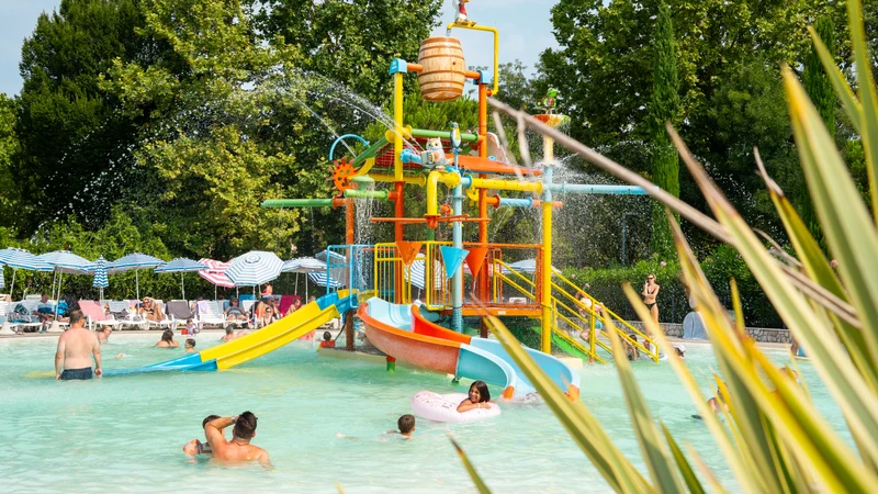 Colorful water playground spraying water, surrounded by children playing in a pool, with trees and loungers nearby at Bella Italia