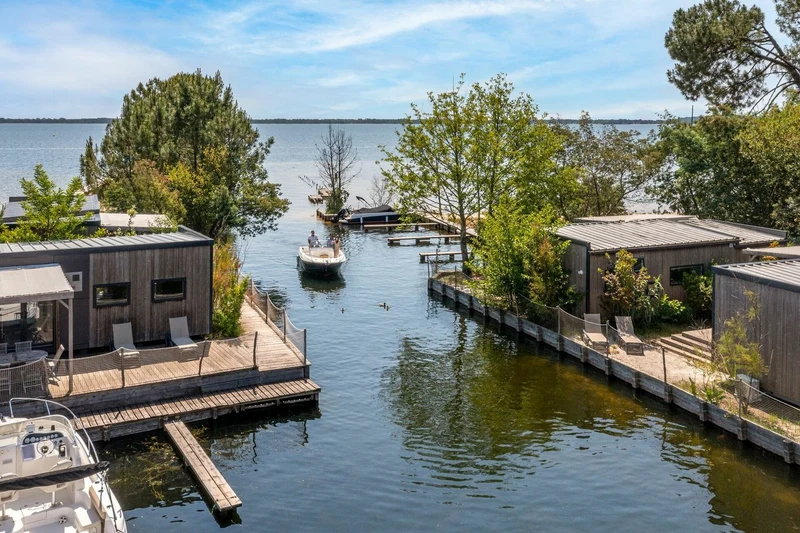 Boat cruising through a canal surrounded by modern wooden cabins and lush greenery at Maguide