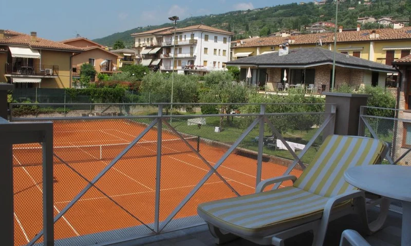 A lounge chair and table overlook tennis courts surrounded by residential buildings and greenery at Hotel Romeo