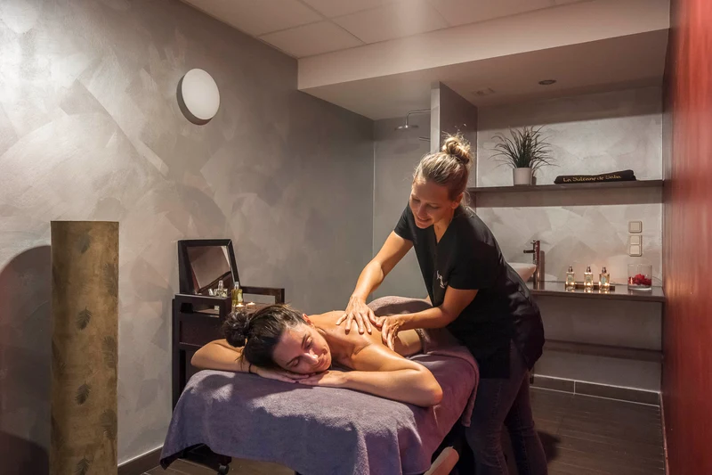 Massage therapist performing massage on a relaxed client in a serene, dimly lit spa room with modern decor at Escale St. Gilles