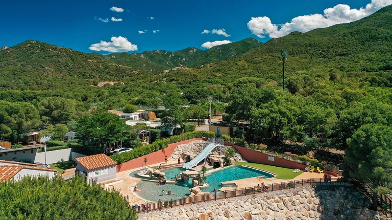 Swimming pool with waterslide surrounded by trees and hills at Les Albères