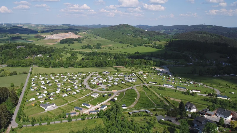 Aerial view of numerous caravans arranged in neat rows on a campsite, surrounded by lush green hills at Brilon