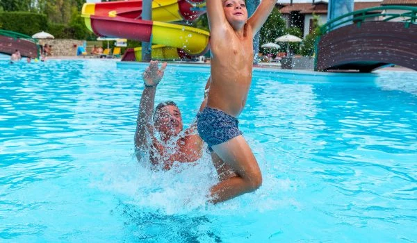 A child jumps from a man's shoulders in a swimming pool with slides in the background at Residence Eden