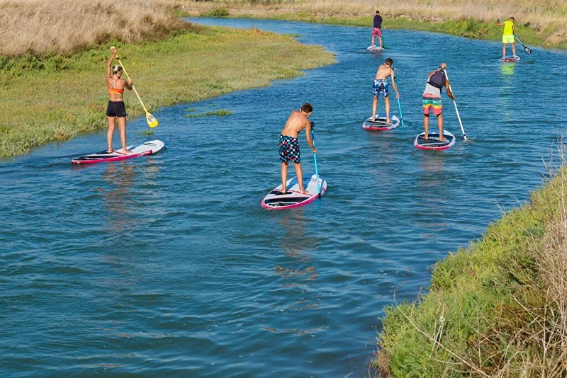 Several people paddleboarding on a narrow river surrounded by grassy banks at Seasonova Ile de Ré