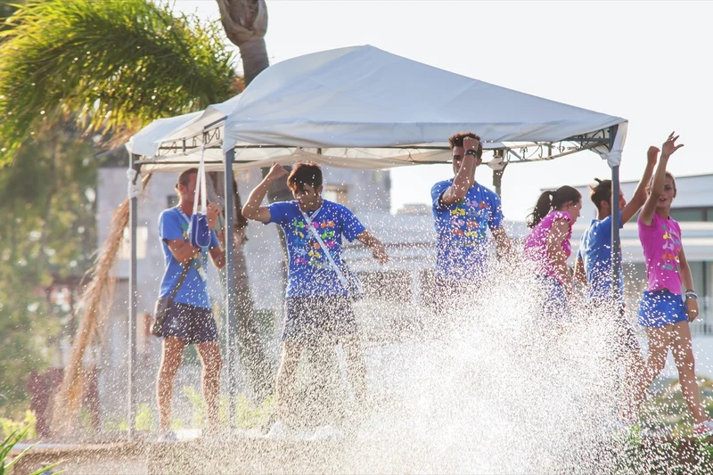 Group of young people dancing under a canopy while water splashes around them at I Turchesi Club Village