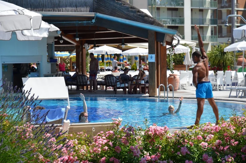 Instructor leading water aerobics in a pool, surrounded by lush flowers and seated people enjoying the sun at Savoy Beach Hotel & Thermal Spa