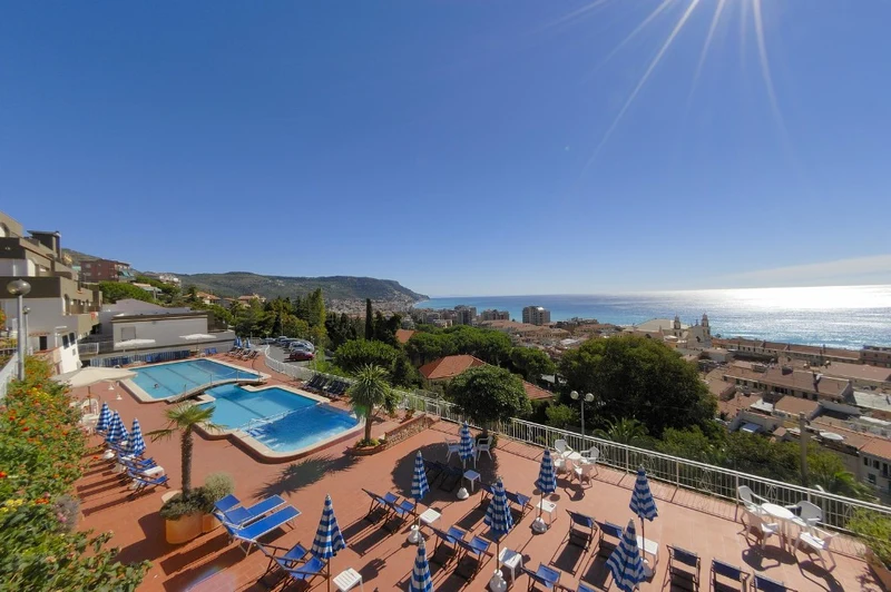Swimming pool area with sun loungers and umbrellas overlooking a coastal city and the ocean at Sant' Anna Residence