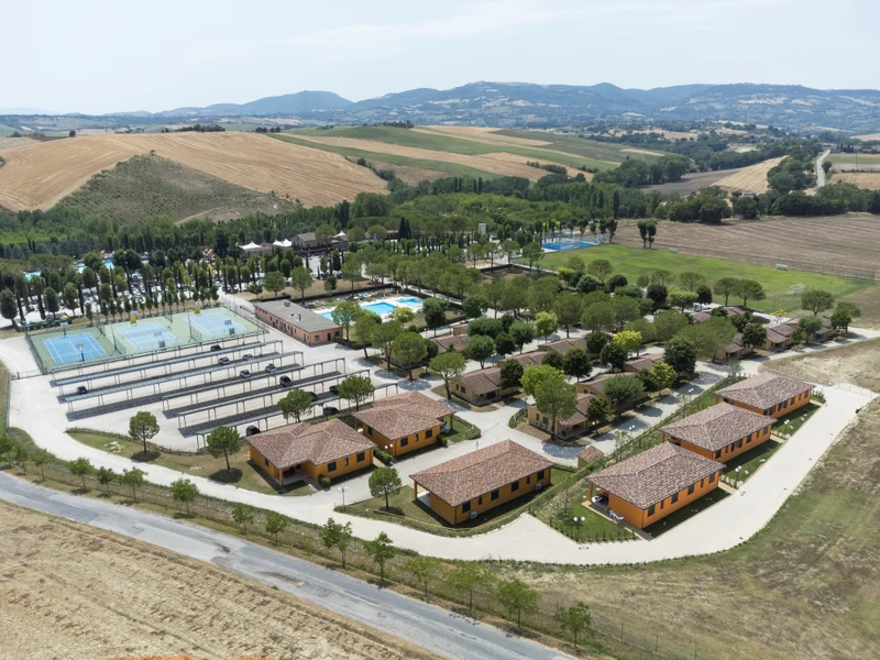 Aerial view of cabins arranged around sports facilities, surrounded by fields and distant mountains and hills at Centro Vacanze Verde Azzurro