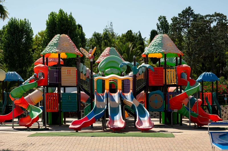 Colorful playground structure with multiple slides and towers, set in a leafy park area at Centro Vacanze Verde Azzurro