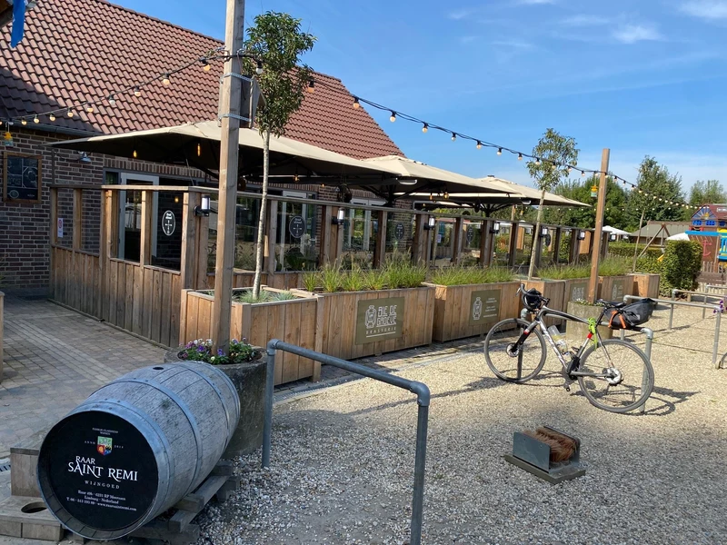 Bicycle parked outside a rustic café terrace with wooden planters, overhanging lights, and nearby playground equipment at 't Geuldal
