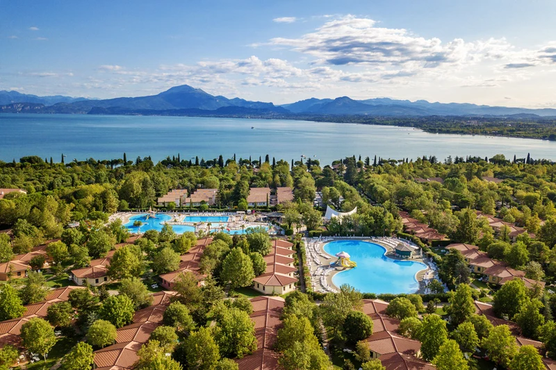 Pools surrounded by greenery and cottages near a lake with mountains in the background at Bella Italia